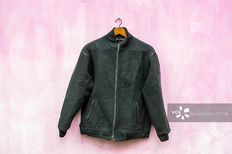 一件深灰色拉链夹克挂在粉色墙上图片素材