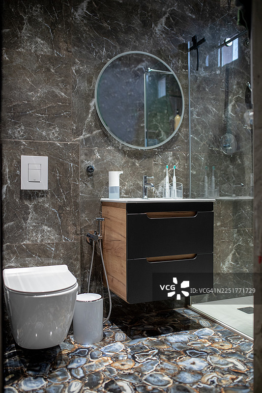 优雅的现代大理石浴室，配有圆形镜子、梳妆台和玻璃淋浴房图片素材