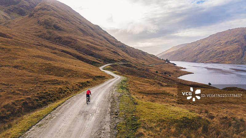 航拍/无人机视角，苏格兰高地一男子沿着湖畔的砂石小径骑行图片素材