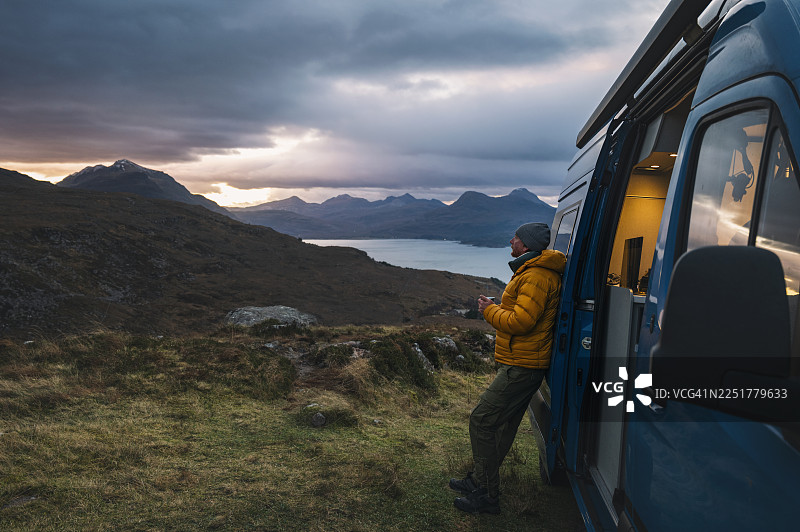 秋日清晨，一位成熟的男士在苏格兰高地欣赏湖泊和山脉的景色图片素材