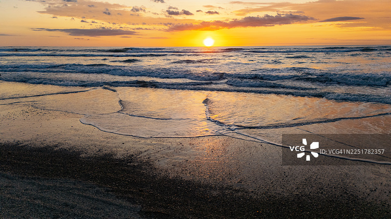 金色日落映照海面，湿沙上留下的倒影图片素材