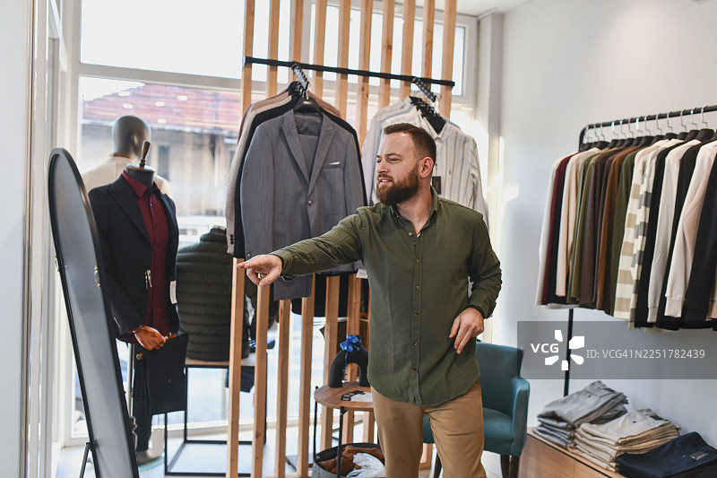 男士在时尚店购物，试穿衣服时指向镜子，寻求新造型图片素材