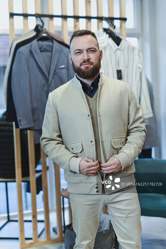 时尚男士身穿米色开衫，置身于挂满西装的服装店中图片素材