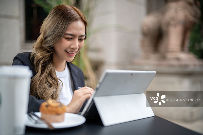 一位亚洲女商人在户外使用平板电脑工作，旁边放着一杯咖啡图片素材