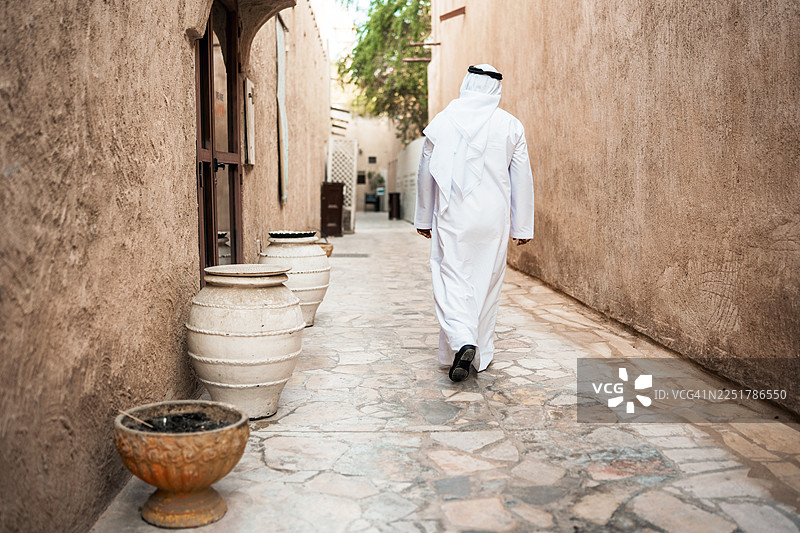 一位年长的导游走在古老的巷道中，这里是传统的Al Fahidi历史街区图片素材