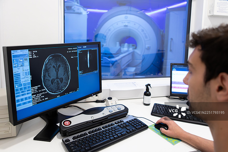 男性放射科技师正在看着他显示器上的不同核磁共振成像，并对其进行分析。图片素材