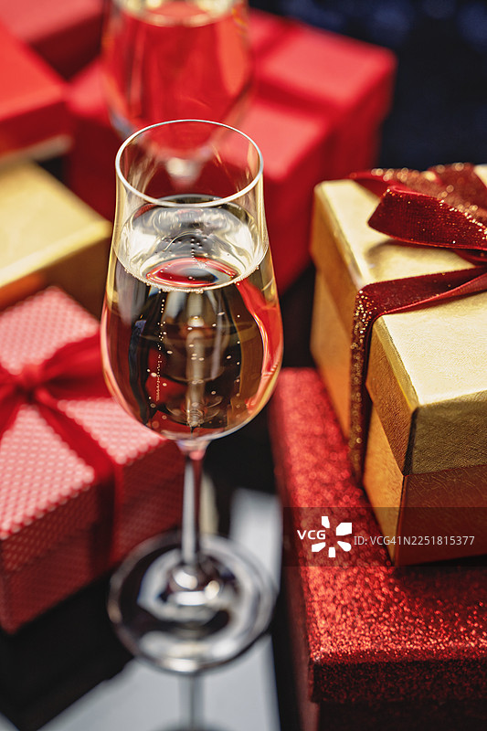 节日蓝色背景上，香槟杯和优雅的金色礼品盒，配有红色丝绒蝴蝶结、金色串灯和闪光散景，供摹仿。图片素材