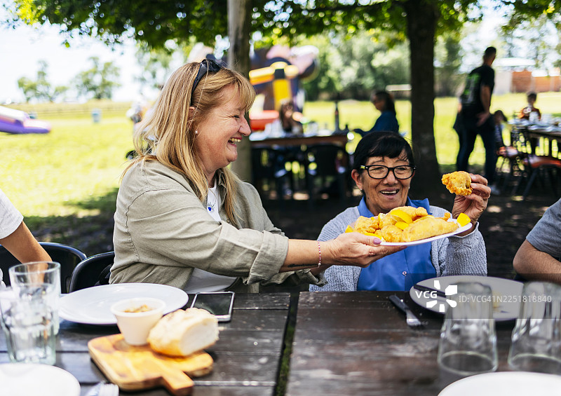 成熟的女性在快乐的户外社交聚会上分享食物图片素材