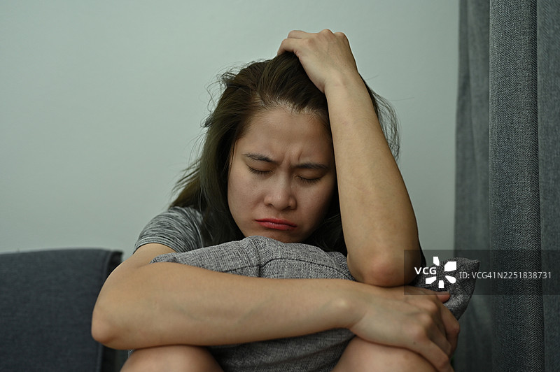 沮丧的女人因为悲伤或心碎而独自坐在客厅里。图片素材