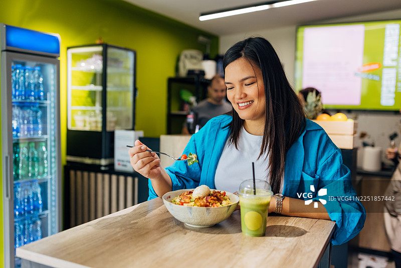 快乐的菲律宾女性，正在享受一顿健康的、恢复活力的、富含蛋白质的沙拉和维生素丰富的绿色果汁/冰沙，享受片刻的宁静。图片素材