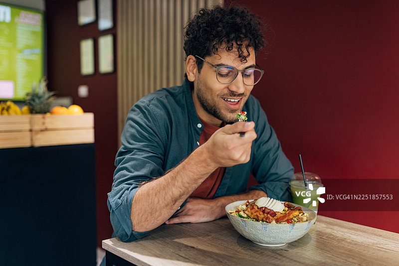 无忧无虑的男人微笑着享用一份高蛋白、营养均衡的沙拉和一杯绿色超级食物冰沙图片素材