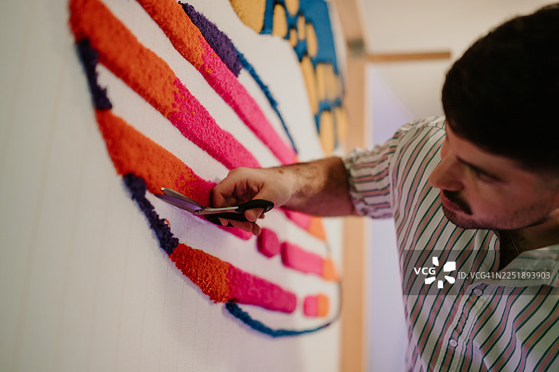 男人用剪刀修剪色彩鲜艳的簇绒地毯艺术品图片素材