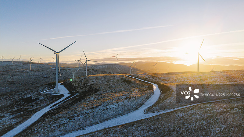 在寒冷冬日日落时分，苏格兰高地山坡上风力涡轮机的广阔航拍/无人机视角图片素材