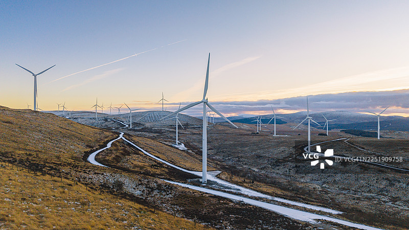 寒冷冬日日落时苏格兰高地山坡上风力涡轮机的宽广航拍/无人机视角图片素材