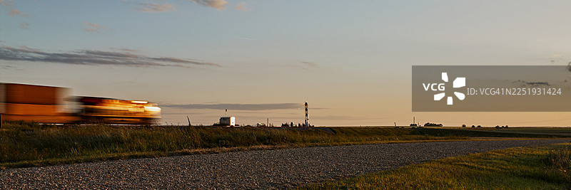 夕阳下，货运火车经过草原上的道路图片素材