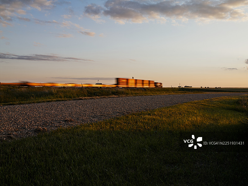 黄昏时分，货运火车经过草原上的公路图片素材