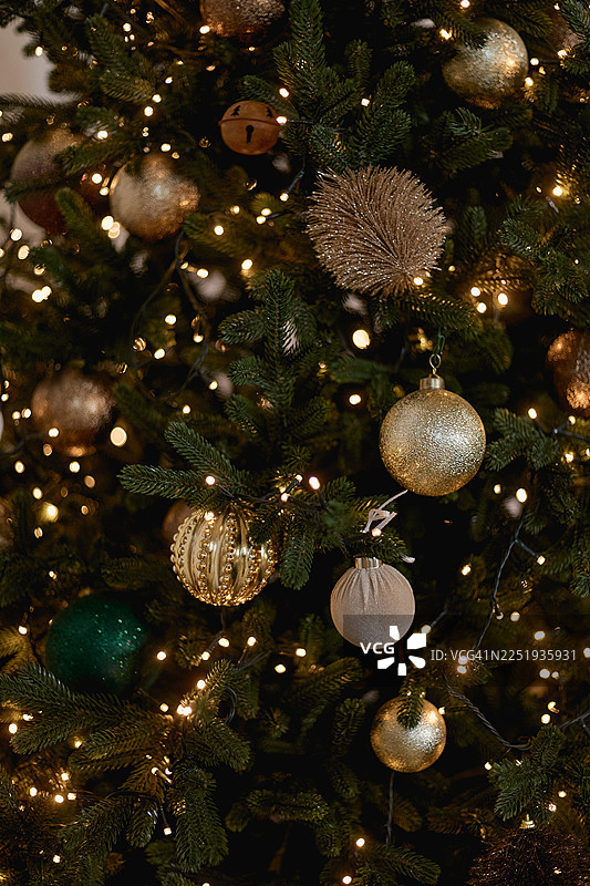一棵圣诞树的特写，上面装饰着金色和绿色的彩球，并由彩灯照亮。图片素材