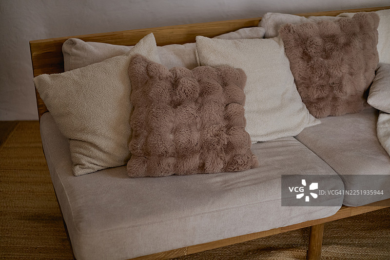 浅木色沙发配着毛绒靠垫，摆放在编织地毯上。图片素材