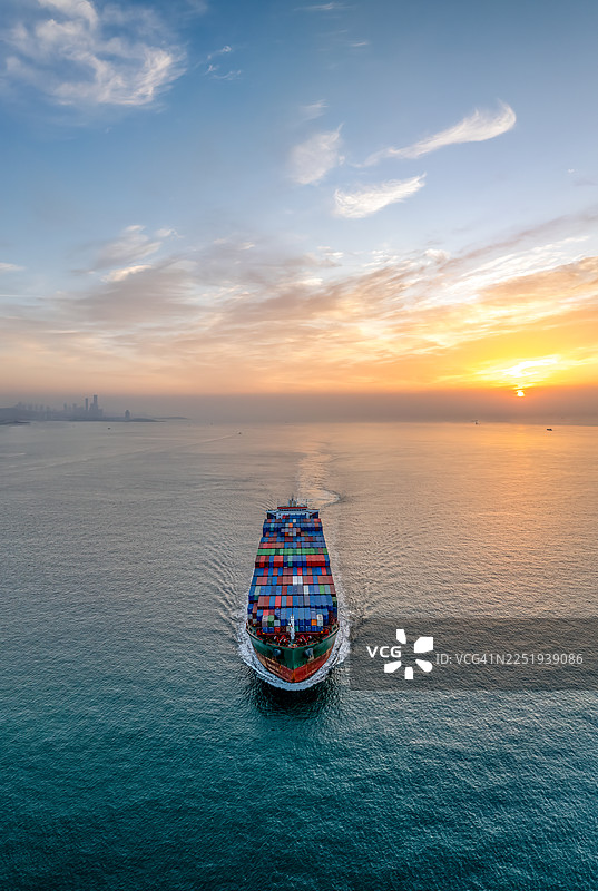 日出时分，无人机航拍视角下的集装箱船航行在美丽的天空和五彩云朵之中图片素材
