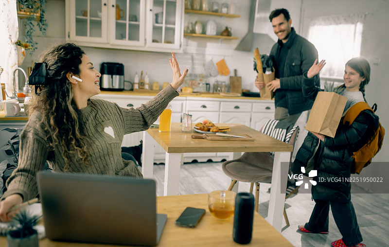 居家办公的母亲与带着食物袋回家的丈夫和女儿互动图片素材