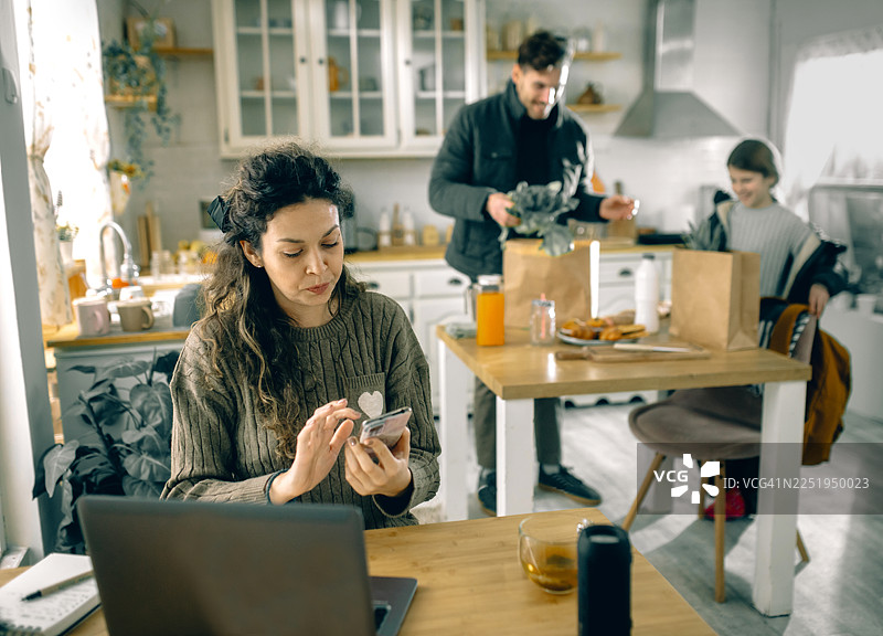 居家办公的妈妈与带着食物袋回家的丈夫和女儿互动图片素材