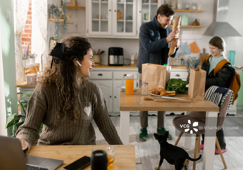 在家工作的妈妈与丈夫以及带着食物袋回家的女儿互动图片素材