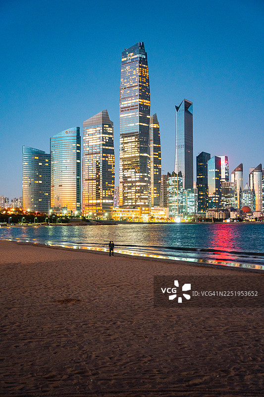 傍晚时分，中国山东青岛第三海滨浴场的都市天际线灯火辉煌。图片素材