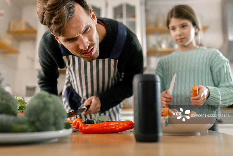 父亲和女儿在烹饪时，向智能语音助手寻求食谱建议图片素材