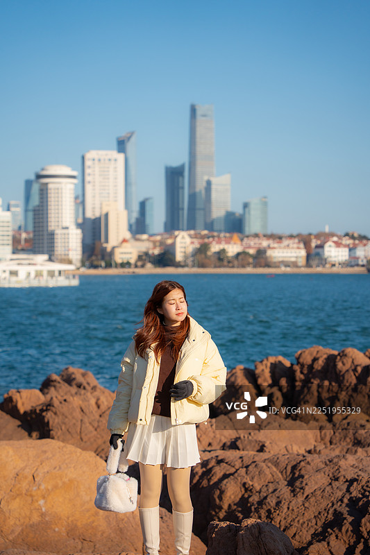 一位美丽的女士站在青岛海滩前，在日落时分欣赏青岛市的美景，地点在山东省青岛市。图片素材