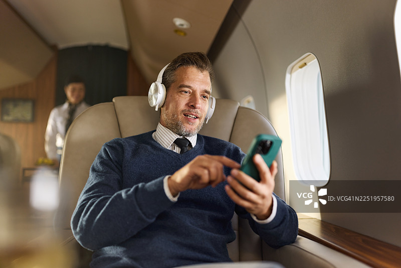 商务人士在私人飞机上通过手机听音乐，面带笑容。图片素材