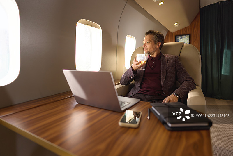 商务人士在私人飞机上享用威士忌，面带笑容。图片素材