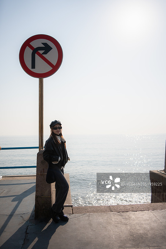 一位美丽的女子站在青岛历史城区天际线附近的水边。图片素材