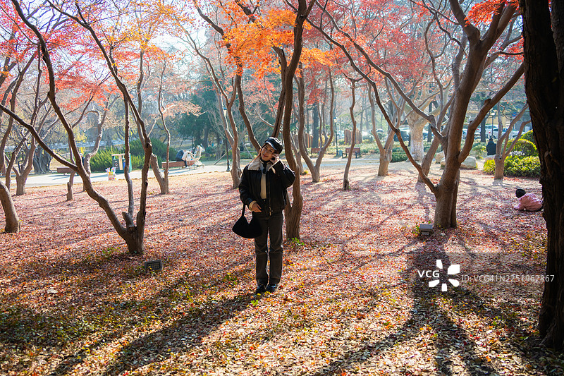 在一个美好的秋日，一位年轻的亚洲女性在公园里悠闲散步，享受着阳光的温暖，呼吸着新鲜的空气，闭着眼睛。在枫树下放松身心。图片素材