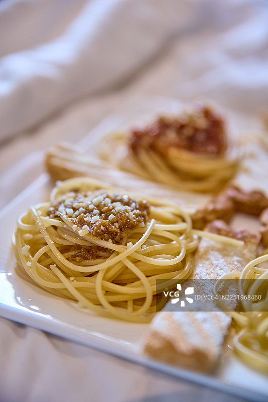 一盘精致的意大利面特写，上面淋着浓郁的肉酱，撒上奶酪碎。图片素材
