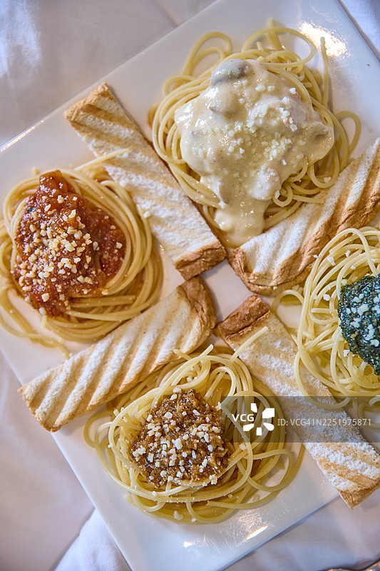 一个方形盘子里装着四种意面：番茄意面、阿尔弗雷多意面、香蒜酱意面和棕酱意面。图片素材