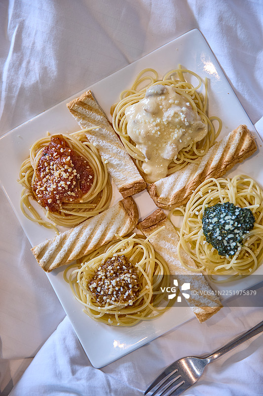 一个方形盘子里装着四种意大利面，分别是番茄酱、阿尔弗雷多酱、香蒜酱和棕色酱。图片素材