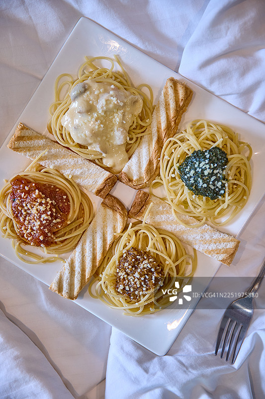 一个方形盘子里装着四种意大利面，分别是番茄酱、阿尔弗雷多酱、香蒜酱和棕酱。图片素材