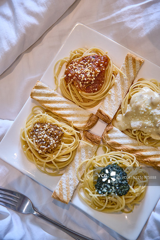 一个方形盘子，盛有四种意大利面食——番茄酱、阿尔弗雷多酱、香蒜酱和棕酱。图片素材