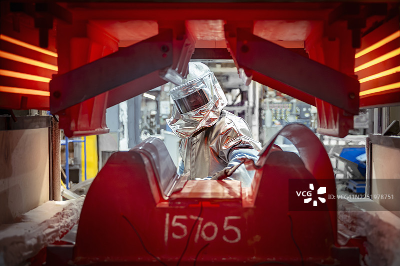 在航空航天零件制造厂，透过高温钛压机视角看身穿隔热服的工程师图片素材