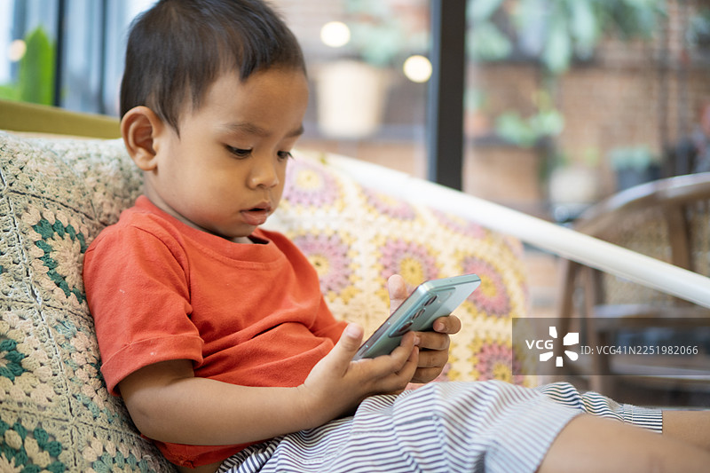 亚洲宝宝在客厅的沙发上玩智能手机图片素材