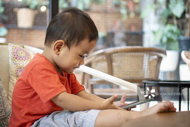 亚洲幼儿在客厅的沙发上玩智能手机图片素材