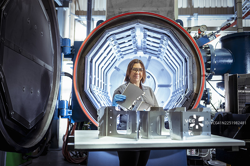 在航空航天零件工厂，工程师在真空热处理炉前检查金属零件图片素材