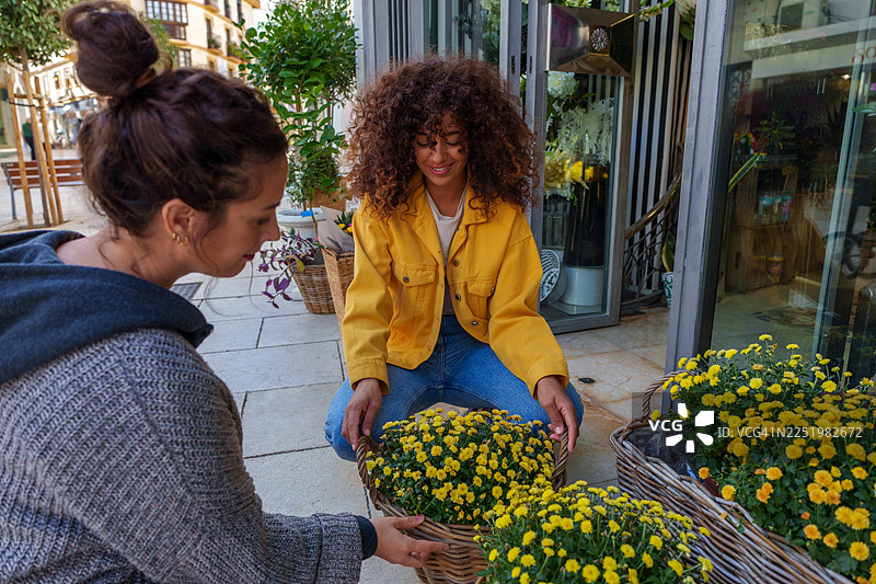 女子在花店外摆放黄色盆栽花卉图片素材