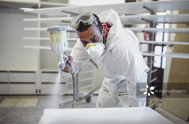 中年多民族男性木匠在室内喷漆木材图片素材