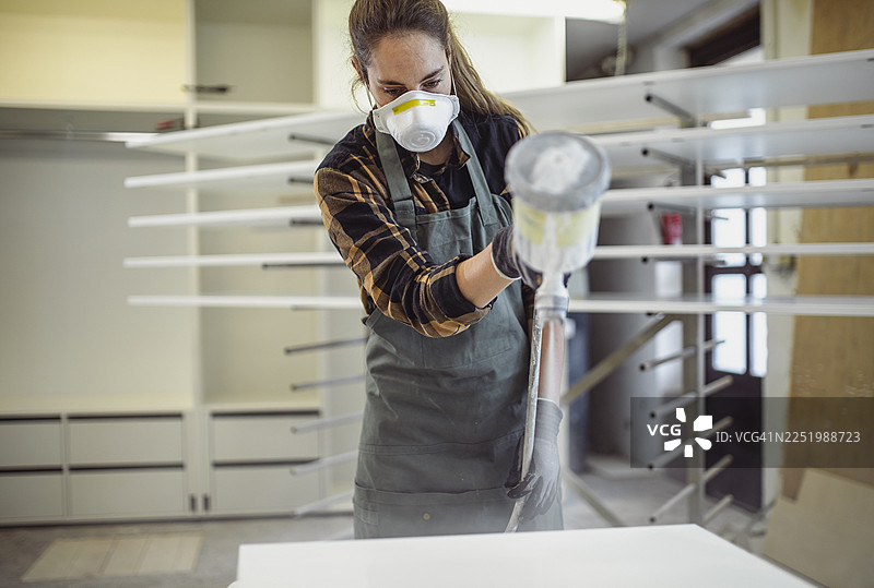 白种女性在工作室给木材喷涂面漆图片素材