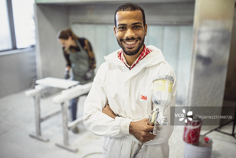 快乐的跨种族男性木匠在工作室里拿着喷漆枪图片素材