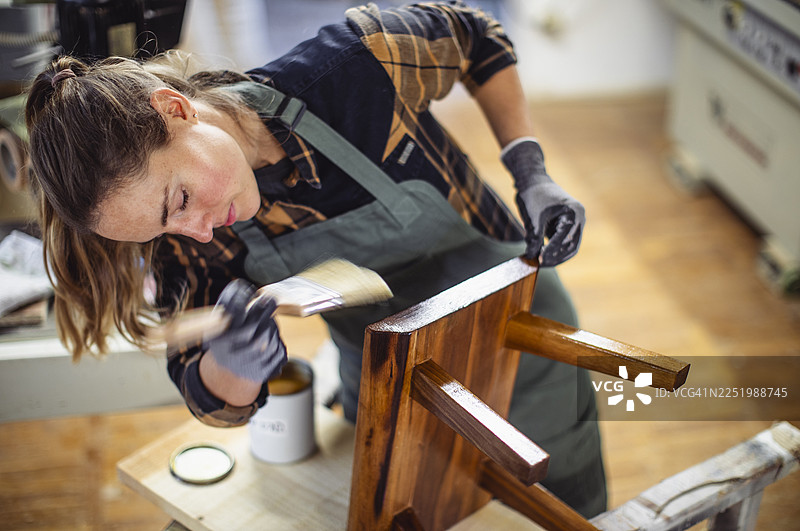 一位高加索女性在工作室里小心翼翼地给木凳上漆图片素材