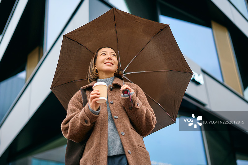 年轻女子撑着伞，手拿外卖咖啡图片素材