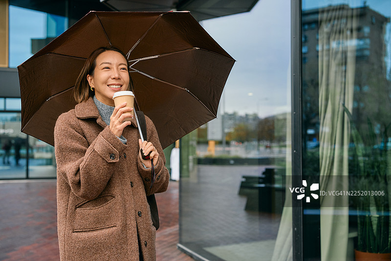 一位女士撑着伞在城市街道上喝咖啡图片素材