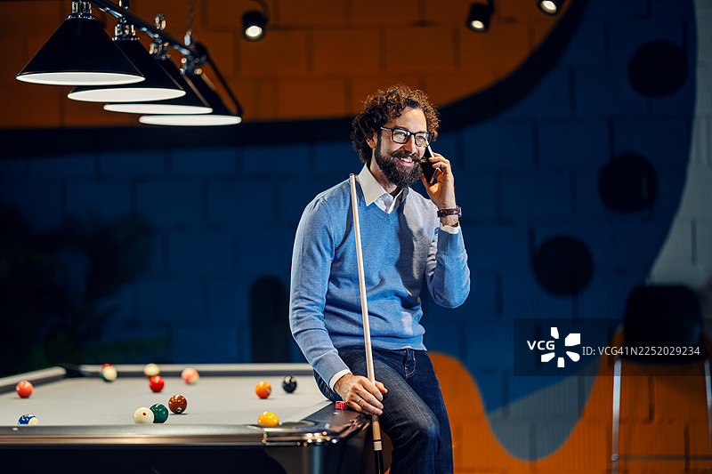 一个男人坐在台球桌上，面带微笑地打电话图片素材